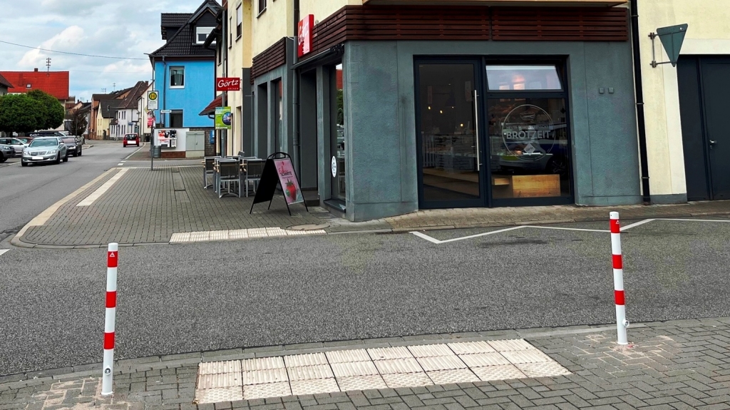 An der Straßenecke Wiesenstraße / Heidelberger Straße wurden zwei rot-weiße Poller gesetzt, um unzulässiges Parken zu verhindern. Hier ist ein traktiles Leitsystem für seheingeschränkte Menschen, das den Straßenübergang sicherer machen soll.