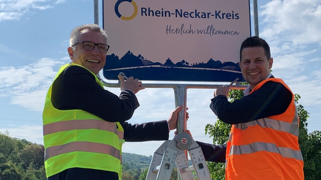 Landrat Stefan Dallinger und Bürgermeister Benjamin Köpfle freuen sich über das erste Willkommensschild im Landkreis. (Bild: Landratsamt Rhein-Neckar-Kreis)