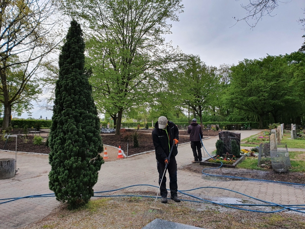 Mitarbeiter bekämpfen Unkraut mit Heißwasser auf dem Friedhof