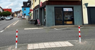 An der Straßenecke Wiesenstraße / Heidelberger Straße wurden zwei rot-weiße Poller gesetzt, um unzulässiges Parken zu verhindern. Hier ist ein traktiles Leitsystem für seheingeschränkte Menschen, das den Straßenübergang sicherer machen soll.