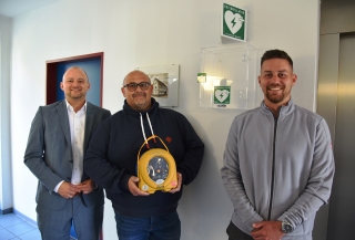 Bürgermeister Pascal Seidel mit Bernd Hertlein und Marcel Pfau vor dem neu installierten Defibrillator im Siegwald-Kehder-Haus.
