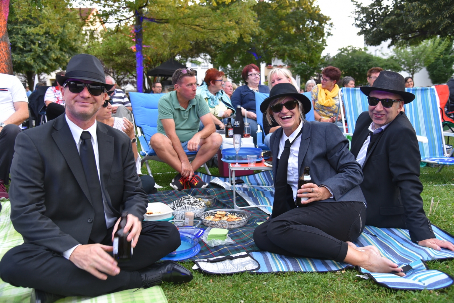 Etliche Besucher*innen sind wie die Blues Brothers in schwarz-weiß gekleidet und tragen Sonnenbrille.