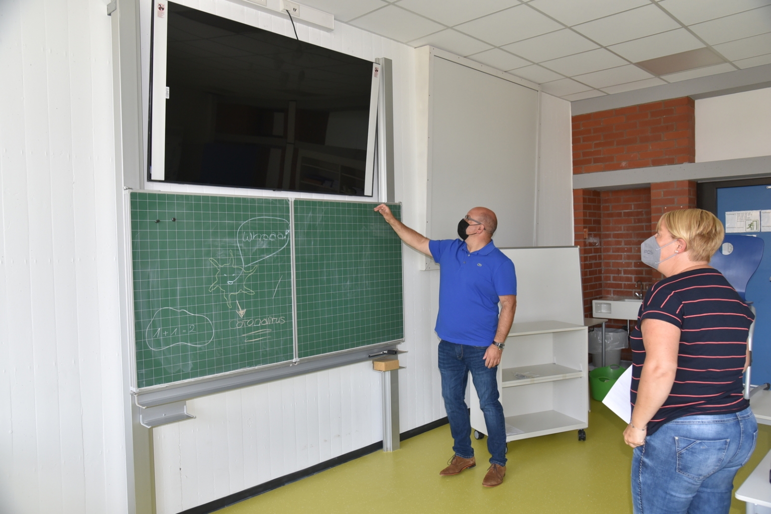 Bürgermeister Jens Geiß testet mit Rektorin Alexa Schäfer den neuen Monitor in einem der neuen Klassenzimmer.